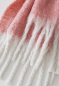 Sciarpa lavorata a maglia con una sfumatura che va dal rosa chiaro al bianco, con frange bianche prominenti, caratterizzata da una consistenza morbida e pelosa.