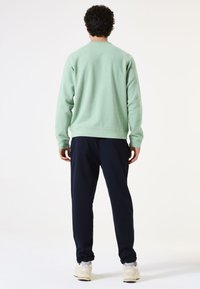 Sudadera verde de algodón con puños y dobladillo acanalados, combinada con pantalones jogger azul marino y zapatillas de color claro. Enfocada en la comodidad y el ajuste casual.