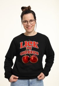 Sudadera negra con texto rojo que dice "LICK my CHERRIES", con dos cerezas rojas brillantes ilustradas debajo del texto.