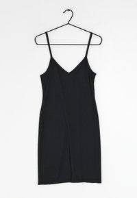 Černé, bezramínkové šaty s tenkými ramínky, navržené ve tvaru písmene V, vyrobené z měkké tkaniny, s přiléhavým střihem a délkou ke kolenům. Visí na černém háčku.