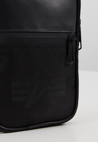 Svart axelväska med en kombination av släta och strukturerade material, dragkedjeficka och logotypdesign med vinklade inslag.