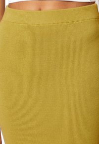 Pletená sukně hořčicové barvy s žebrovanou strukturou, která má široký elastický pas pro pohodlí a přiléhavý střih.