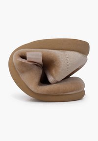 Chausson pliable beige avec une tige douce et texturée, doublure lisse et semelle en caoutchouc flexible. Dispose d'une petite boucle en tissu pour une prise en main facile.