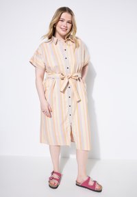 Abito a camicia a righe nei colori pastello con cintura legata, maniche corte e bottoni neri. Indossato con sandali rosa con elementi decorativi.