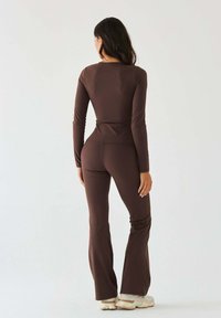 Brązowa bluzka z długim rękawem i dopasowane rozszerzane spodnie z gładkiej tkaniny. Posiadają wysoki stan i prosty, elegancki design. Białe sneakersy.