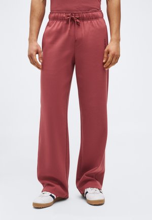 Azúrkék laza, márványos, zsinóros nadrágot és fehér gumitalpú sportcipőt viselő férfi, aki egy egyszerű világos háttér előtt áll.