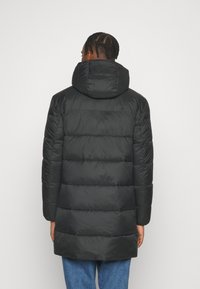 Schwarzer Steppmantel mit hohem Kragen, gesteppter Optik und langen Ärmeln. Glatte Textur und mittellanger Schnitt, geeignet für kaltes Wetter.