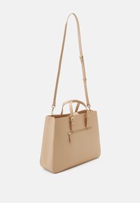 Sac fourre-tout en synthétique beige avec une forme structurée, deux poignées supérieures, une bandoulière réglable et une poche zippée à l'avant avec quincaillerie dorée.