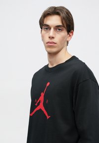 Μαύρη φούτερ από βαμβάκι με γραφικό λογότυπο Air Jordan σε κόκκινο χρώμα που βρίσκεται στο κέντρο του στήθους. Διαθέτει στρογγυλή λαιμόκοψη και χαλαρή εφαρμογή.