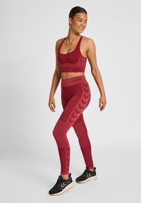 Reggiseno sportivo rosso e leggings con motivi a zigzag, tessuto elasticizzato, design aderente e abbinati a scarpe da ginnastica nere.