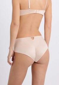Sous-vêtements pour femmes beige clair avec une texture lisse, présentant un design taille basse et une découpe décorative à l'arrière. Bretelles ajustables sur le soutien-gorge assorti.