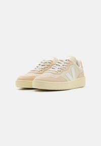 Beige semsket og skinn sneakers med hvite detaljer, perforerte detaljer og lysegrå snørebånd. Flat gummisåle. Minimalistisk design.