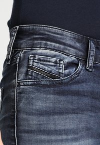 Donkerblauwe denim jeans hebben een vervaagd ontwerp met zichtbare stiksels, een klein voorvak en een onderscheidende stofstructuur.