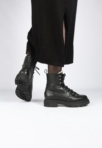 Zwarte leren veterlaarzen tot de enkel met een grove zool, voorzien van metalen veteroogjes, een gestructureerde afwerking en een verstevigde hiel voor ondersteuning.