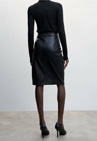 Haut noir à manches longues associé à une jupe crayon en cuir noir, avec une texture lisse et une silhouette ajustée, complété par des talons hauts.