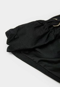 Czarna opaska na głowę z marszczoną fakturą i srebrnym metalowym pierścieniem na białym tle.