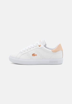 Witte lage sneaker met perzikkleurig hielstuk, roségouden krokodillenlogo aan de zijkant, witte veters en reliëf Lacoste-merk op de zool.