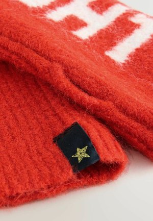 pulover tricotat roșu cu model alb, având textură ribbată și o etichetă țesută cu un accent de stea aurie. Material moale și pufoș.