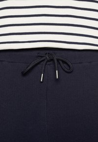 Gros plan d'un pantalon bleu marine avec un cordon noir noué et une chemise blanche avec des rayures horizontales noires au-dessus de la ceinture.