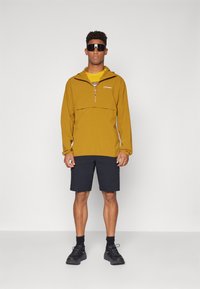 Pulóverová bunda v horčicovo žltej farbe, so zipsom po polovici, prednou vreckom a logom. V kombinácii s tmavými cargo šortkami a čiernymi top�ánkami.