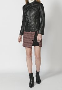 Czarna skórzana kurtka z zamkiem z przodu, zestawiona z czerwoną i czarną spódnicą w kratę z bocznym guzikiem. Czarne botki za kostkę.