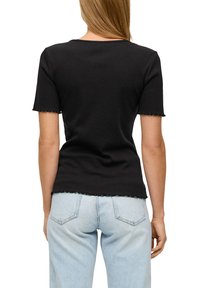Zwarte t-shirt met korte mouwen en een golfrand, met een aansluitend ontwerp. Gecombineerd met lichtblauwe hoge taille jeans.