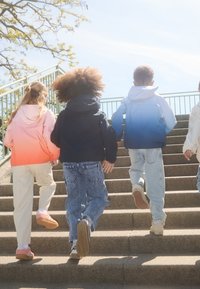 Quatre enfants montent des escaliers extérieurs, portant des vestes à capuche colorées, des jeans et des chaussures légères. Les vestes vont d'un dégradé rose à bleu.