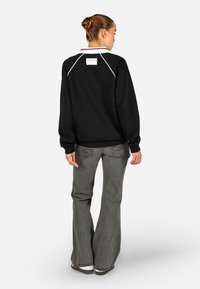 Μαύρο φούτερ με λευκή ραφή, ριγωτούς μανσέτες και ψηλό γιακά, σε συνδυασμό με γραμμή παντελόνια σε γκρι απόχρωση με κεντημένα πίσω τσέπες.