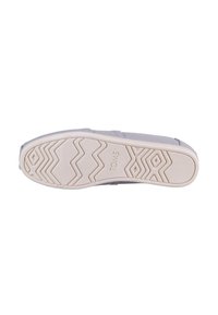 Sneaker in tessuto grigio chiaro con una suola in gomma bianca testurizzata, caratterizzata da motivi a zigzag e con il nome del marchio "TOMS" impresso sul lato.