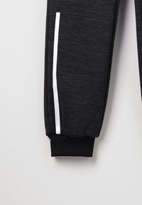 Schwarze sportliche Jogginghose aus strukturiertem Stoff, mit elastischen Säumen und einem weißen Streifen, der das Bein akzentuiert.