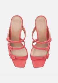 Koralowe zamszowe sandały na wysokim obcasie z kwadratowym noskiem i trzema regulowanymi paskami z klamrami. Gładkie wewnętrzne wykończenie oraz solidne słupkowe obcasy.