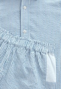 Svijetloplava i bijela košulja s prugama, s kopčanjem na prednjoj strani, mekanim materijalom, volančićima na rubu i džepom s flasterom. Prugama su ravnomjerno raspoređene.