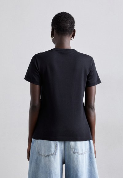 T-shirt preto de manga curta com decote redondo; material de algodão macio; textura suave; design simples e funcional; usado com denim azul claro.