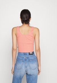Débardeur côtelé rose clair avec un col arrondi, associé à un jean en denim bleu taille haute avec une étiquette au dos.