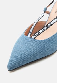 Μπλε τζιν παπούτσι μπαλαρίνα με μυτερή μύτη και μαύρα και λευκά λουράκια με το λογότυπο "LOVE MOSCHINO" που διασταυρώνονται στον πάνω μέρος του ποδιού.