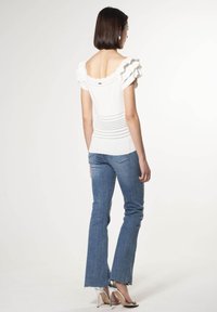 Witte top met gerimpelde mouwen en open rug, met een stippenpatroon nabij de zoom. Gecombineerd met lichtblauwe flared jeans en zilveren hakken.