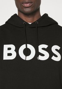 Felpa nera con cappuccio e un grande logo bianco "BOSS" sul davanti, caratterizzata da un cappuccio con cordino e una texture morbida e liscia.