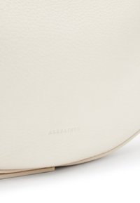 Borsa a tracolla in pelle crema con una superficie texture, caratterizzata da un sottile logo "ALLSAINTS" impresso vicino al fondo e dettagli lisci di colore beige.