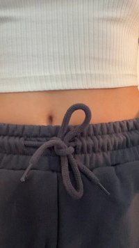 Grå joggebukser med teksturert midjebånd, som har en knyttet detalj. En hvit ribbet crop top er synlig over buksene.