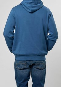 Sudadera azul con capucha y dobladillo y puños acanalados, combinada con jeans de mezclilla azules, vista desde la parte trasera. Textura suave, ajuste casual.