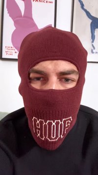 Bordó kötött balaklava, szemnyílásokkal és világosbarna 'HUF' logóval, fekete pulóverrel párosítva. A textúra bordázott és szoros.
