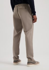 Pantaloni bej cu talie elastică, slim fit și două buzunare la spate. Textură de țesătură netedă, asortați cu încălțăminte casual.