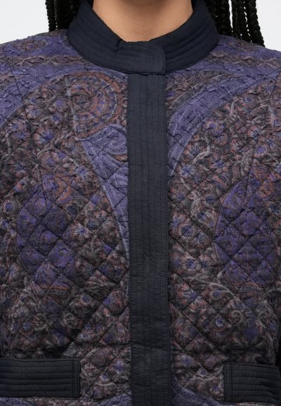 Μπουφάν με καπιτονέ ύφασμα και σχέδιο παϊέντζα σε αποχρώσεις μοβ και μαύρου, με ψηλό γιακά και αντίθετη σκουρόχρωμη επένδυση κατά μήκος του εμπρός μέρους.