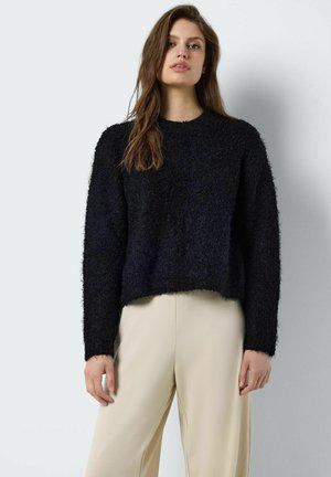 Zwarte, donzige gebreide trui met een ronde hals en lange mouwen, cropped ontwerp, gedragen over beige, losvallende broek.