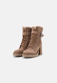 Bottes chelsea en suede marron avec un dessus texturé matelassé, un devant lacé, un col en fourrure douce et un talon épais. Accentué de clous et d'une sangle.