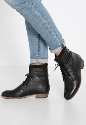 Bottines en cuir noir à lacets avec de petits talons en bois portées avec un jean en denim bleu clair retroussé.