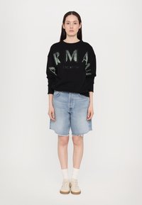 Čierna mikina s tlačeným zeleným logom "ARMANI EXCHANGE"; svetlomodré džínsové šortky s rozstrapkaným lemom; krémové tenisky a biele ponožky.