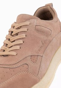 Beige mockaskor med rund tå, snörning framtill, perforerade detaljer och texturerad gummisula. Logotyp präglad på sidan.