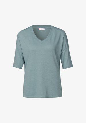 Světlá tyrkysová halenka s krátkým rukávem a výstřihem do V. Měkká, texturovaná látka, volný střih a mírně spadlé ramena. Viditelný štítek značky.