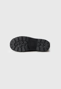 Suela de zapato de goma, negra, con un patrón de agarre texturizado y un diseño de tracción moldeado que presenta seis formas estelares y un logo rectangular.